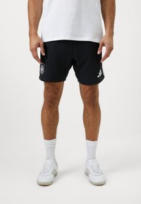 Calções de desporto pretos com um logótipo redondo na perna esquerda e riscas brancas da Adidas nas laterais, feitos de um tecido de algodão macio.