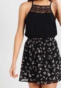 Abito nero con corpino in pizzo e spalline regolabili, caratterizzato da una gonna svasata decorata con una stampa floreale multicolore su sfondo nero.