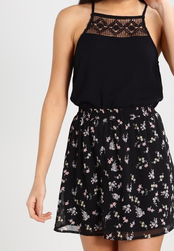 Abito nero con corpino in pizzo e spalline regolabili, caratterizzato da una gonna svasata decorata con una stampa floreale multicolore su sfondo nero.