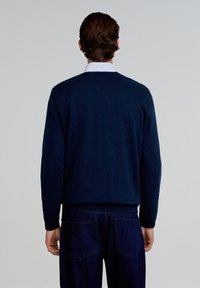 Pull marin à col rond en tissu doux, avec des manches longues et des poignets côtelés, associé à un jean en denim foncé avec des poches arrière.