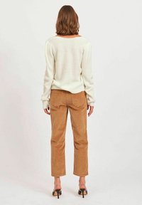 Jersey de canalé crema con escote amplio, combinado con pantalones de pana color beige y sandalias de tacón negras. La vista trasera muestra los materiales texturizados.