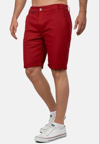 Rode katoenen shorts met gerolde manchetten, voorzakken en een knoopsluiting. Heeft een klein logo op de tailleband.