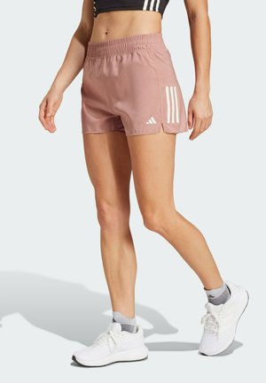 Shorts sportive roz cu un brâu elastic, având dungi diagonale albe pe lateral și tivuri despicabile pentru mobilitate. Pantofi de alergare albi.