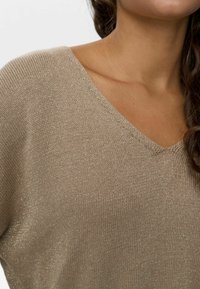 Beige V-kaelusega kudum, millel on kerge tekstuuriga kangas, mis sisaldab peent sära. Looduslik istuvus langenud õlgadega ja soonikkoes detailidega.