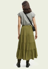 Falda larga de corte en capas en verde oliva con cintura elástica, combinada con una camiseta gris de manga corta y un bolso de hombro negro, llevada con botas negras de tobillo.
