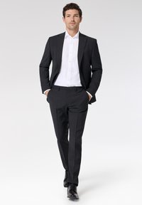 Ciemnoszary, dopasowany garnitur z klapami, zestawiony z białą koszulą na guziki. Slim-fit spodnie mają gładką teksturę, dopełnione czarnymi butami.