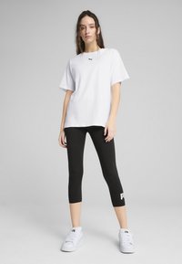 T-shirt en coton surdimensionné blanc avec un détail de logo noir, associé à un legging cropped noir avec des lettres de logo blanches, et des baskets blanches.