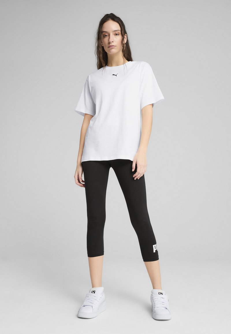 T-shirt en coton surdimensionné blanc avec un détail de logo noir, associé à un legging cropped noir avec des lettres de logo blanches, et des baskets blanches.
