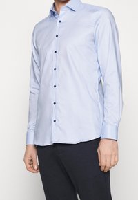 Light blue button-up shirt with blue buttons, long sleeves, and a slim fit. Features a textured pattern and contrasting collar and cuffs.