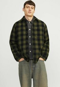 Roheline ja must ruuduline flanellist särk, millel on nööbid ees, rinna tasku ja musta denimi sisemise kihina. Kanda lahtiste teksadega.