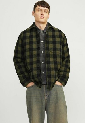 Grøn- og sortternet flannel skjorte med knaplukning fortil, brystlomme og et sort denim indre lag. Båret med løse jeans.