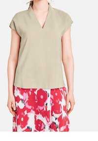 Ljusgrön kortärmad topp med V-ringning, mjuk textur, bärs över en rosa och vit blommönstrad kjol med djärva röda detaljer.