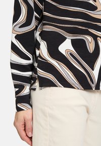 Black top with abstract white, gray, and tan wavy patterns, featuring long sleeves and a relaxed fit. Smooth texture. Lightweight fabric.