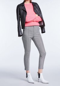 Zwarte leren bikerjack, pluizig roze trui, op maat gemaakte houndstooth broek en witte enkellaarsjes met zwarte accenten.