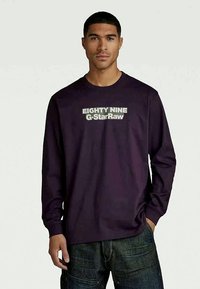 Long-sleeve purple shirt featuring "EIGHTY NINE G-StarRaw" in bold white text across the chest, with a relaxed fit and crew neckline.