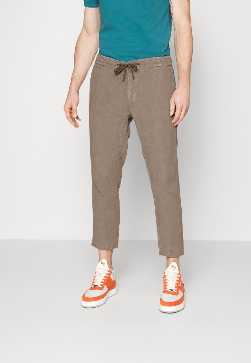 Bruna, lätta linbyxor med dragsko i midjan, taperad ben och en slät textur, ihop med orangea och vita sneakers.