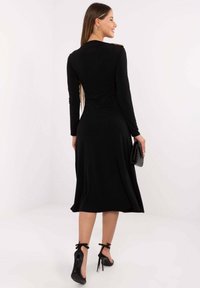 Czarna sukienka z długim rękawem, dopasowaną górą i rozkloszowanym dołem. Złote akcenty na ramieniu. Noszona z czarnymi szpilkami.