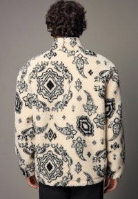 Cremefarvet fleece-pullover med et sort paisley- og diamantmønster, høj krave og struktureret stof. Blødt materiale med en afslappet pasform.