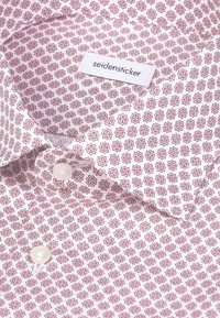 Chemise blanche avec motif étoile géométrique rouge, boutons en perle et une étiquette cousue sur le col portant l'inscription "seidensticker".