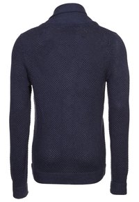 Mörkblå stickad tröja med strukturerat mönster, långa ärmar och uppvikt krage. Bakifrån syns ribbad fåll och mudd.