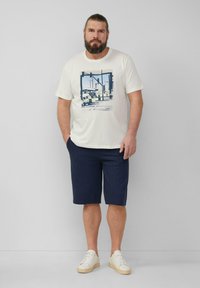 Cream t-shirt with a blue graphic print, paired with navy striped shorts and white sneakers. Casual, relaxed fit throughout.