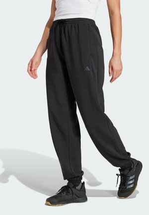 Black athletic pants with an elastic waistband, side zipper pockets, and tapered legs. Features a reflective logo on the left thigh.
