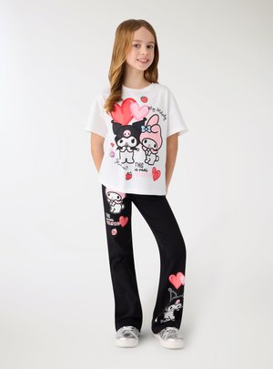 Dziewczyna stoi w białym i czarnym stroju z postaciami z sercami, truskawkami i napisem „To prawdziwa przyjaźń.”