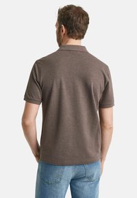 Brun kortärmad pikétröja i mjukt tyg, med klassisk krage och rak fåll, i kombination med ljusblå jeans.