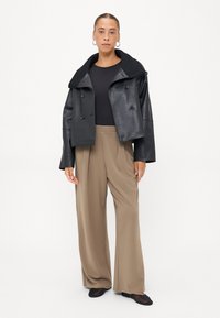 Zwart faux leren cropped jack met een brede kraag, dubbele knopen en een zachte textuur, gecombineerd met beige wijde broek.