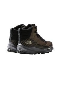 Hiking boots in dark green and black synthetic material, featuring textured upper, padded collar, and rugged sole with pronounced treads.
