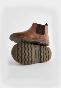 Bruna läder Chelsea-boots med elastiska sidopaneler, askgrå gummisula och kontrasterande söm på vit bakgrund.