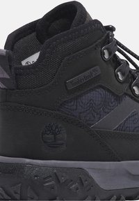 Černé boty Timberland s texturovaným svrškem, gumovou podrážkou, kovovými očky a voděodolným logem na boku. Akcenty s vzorovaným designem.