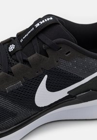 Scarpa sportiva nera con tomaia in mesh, dettagli sintetici, logo swoosh bianco e colletto imbottito per il comfort, progettata per un uso sportivo.