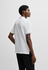 White polo shirt in textured fabric, short sleeves, and a folded collar. Features side slits at the hem and a straight cut design.