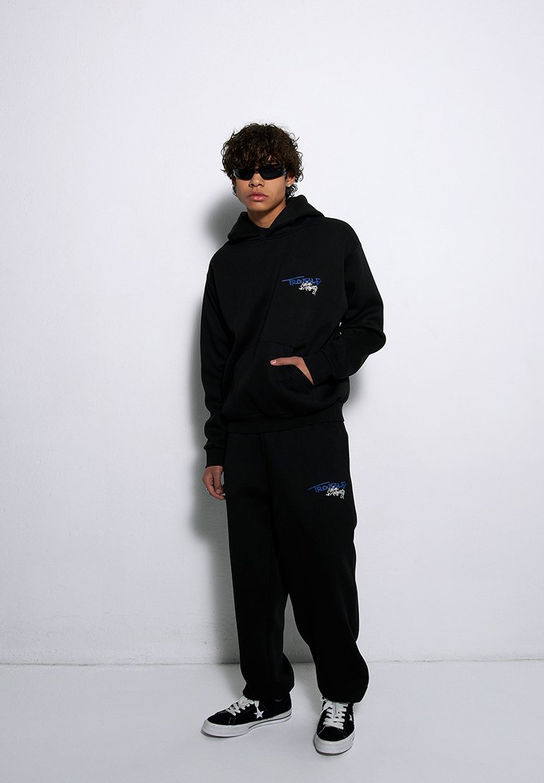 Czarny zestaw z kapturkiem i spodniami dresowymi z kieszenią z przodu. Niebieski nadruk graficzny na obu elementach. Uzupełniony czarnymi trampkami z białymi akcentami.