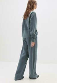 Miętowa, oversize'owa bluza i szerokie spodnie z miękkiego materiału. Bluza ma okrągły dekolt i szew z tyłu; spodnie mają boczne paski.