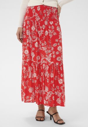 Jupe longue rouge à fleurs avec taille smockée, portée avec des sandales à talons noires à lanières et un haut à manches longues côtelé crème.