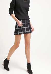 Mini falda de cuadros negra con patrón de rejilla blanca, hecha de tejido texturizado. Combinada con un suéter negro texturizado y botas negras hasta el tobillo.