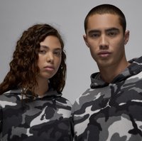 Kamuflage-hoodies i nuancer af grå og sort, med et hvidt logo på brystet. Stofstrukturen ser blød ud med et afslappet pasform-design.