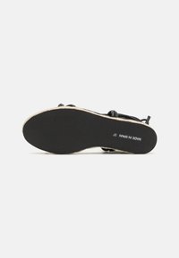Sandal nero con suola in gomma testurizzata e design della fascia intrecciata. Presenta un accento chiaro attorno alla suola. Taglia 37.