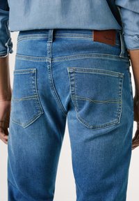 Jeans in denim blu sbiadito con una vestibilità dritta, dotati di due tasche posteriori con cuciture gialle e un'etichetta del marchio in pelle marrone.