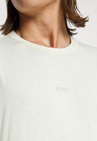 Jasnobeżowa koszulka z krótkim rękawem wykonana z miękkiego materiału, z zaokrąglonym dekoltem i subtelnym wytłoczonym logo "BOSS" na piersi.