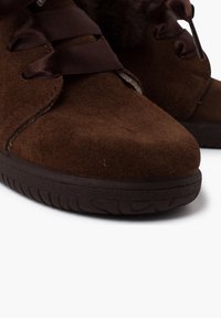 Stivaletti in suede marrone con lacci in satin, superficie testurizzata, punta arrotondata e suola in gomma. Dettagli pelosi lungo il bordo superiore.