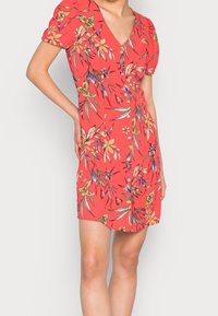 Robe florale rouge avec un décolleté en V, des manches courtes bouffantes et un devant à boutons, ornée d'un motif de fleurs jaunes et bleues ainsi que de feuilles vertes.