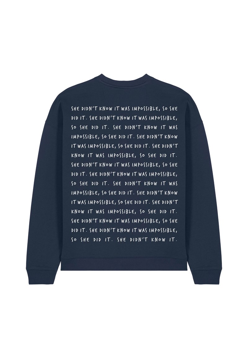 Sweat-shirt bleu marine à manches longues, avec un texte blanc répétitif dans le dos qui parle de surmonter les impossibilités.
