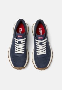 Sneakers in suede blu navy con lacci bianchi, dotati di una intersuola crema e suola in gomma marrone. Etichette rosse "CAMPER" sulla linguetta e sulla soletta.