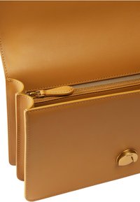 Borsa a mano in pelle color cuoio con un design elegante e strutturato. Presenta una tasca con zip, una texture liscia e un accento metallico con il nome del marchio.