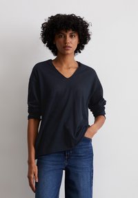 T-shirt in cotone nero con scollatura a V, maniche lunghe, vestibilità comoda e texture delicata; abbinato a jeans in denim blu scuro.