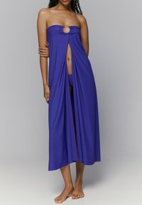 Cubierta morada sin tirantes con un corte ovalado en el centro, que presenta un diseño fluido y dos aberturas laterales. Tela suave y ligera.