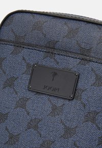 Tessuto blu a motivo con un delicato design di stelle, con una targhetta rettangolare nera con il marchio "JOOP!" impresso e accessori decorativi.